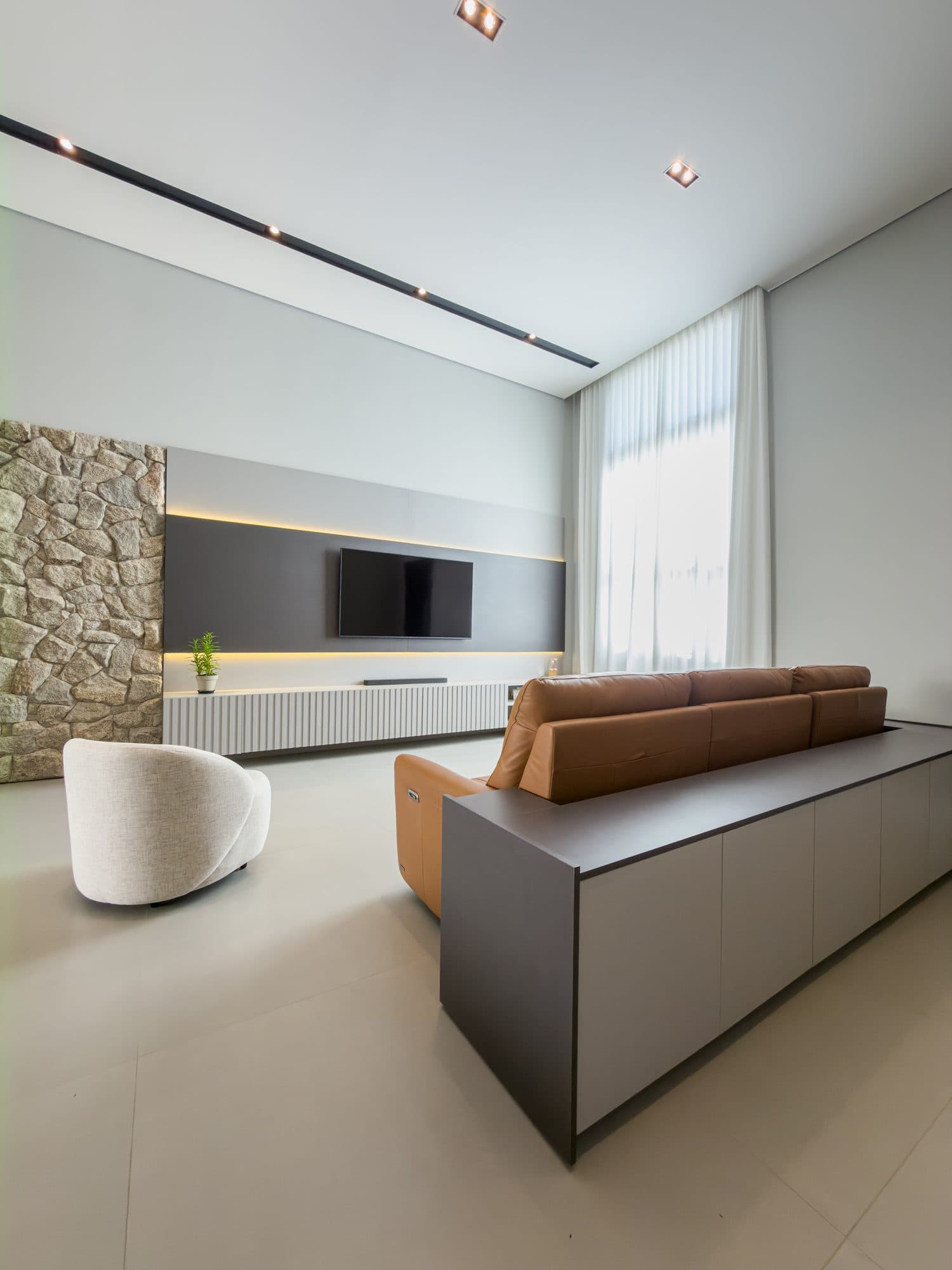 Living com painel para TV em madeira ripada e pedra